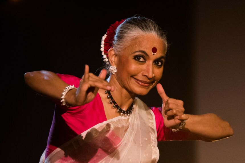 A woman in classical Indian dance dress gestures with her hands and fingers and smiles.
