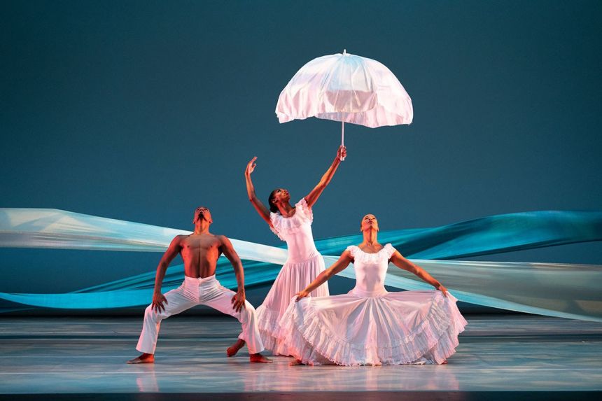 Three Black dancers stand in rigid, muscular poses as they all look upward.