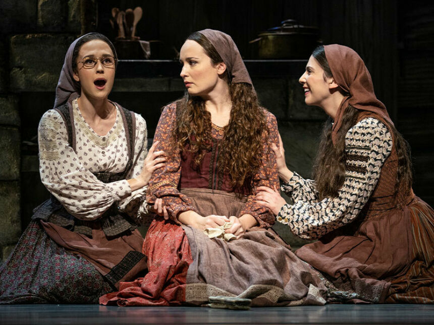Three young women wearing folksy dresses and handkerchiefs on their heads sing.
