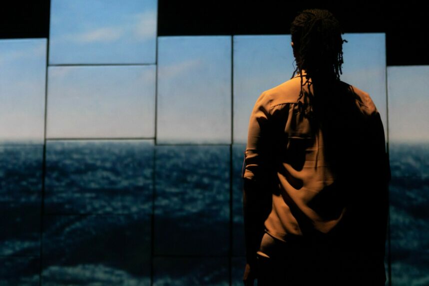 A person stands in front of a wall of monitors broadcasting an ocean scene.