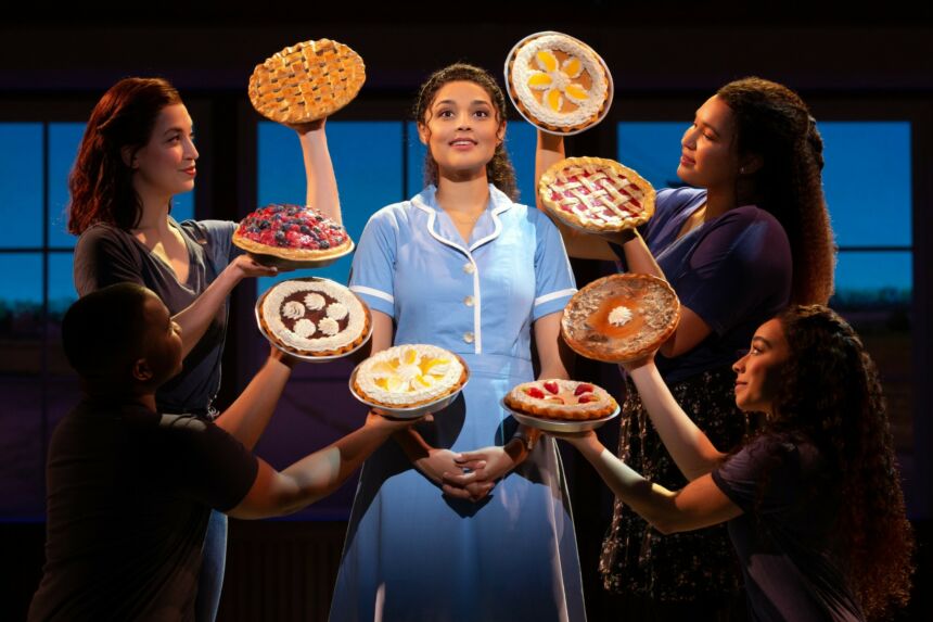A woman dressed in a server's uniform is surrounded by women holding fresh baked pies.