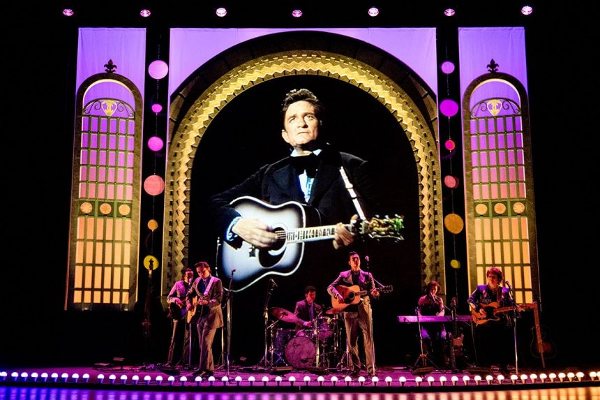 Johnny Cash is shown on a large videoscreen while a group of musicians perform live on the stage.