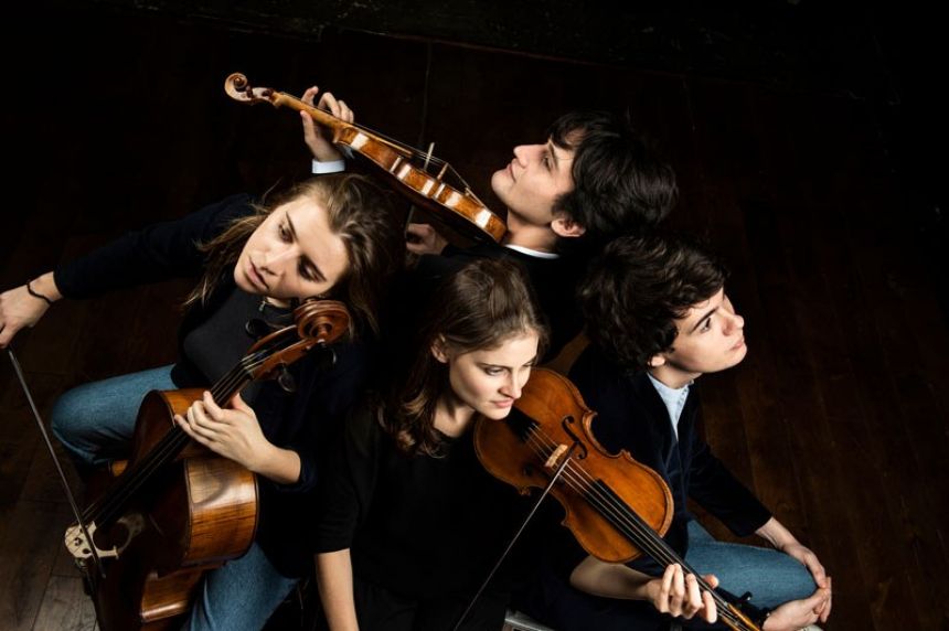 Four White young people stand together and hold their classical string instruments.