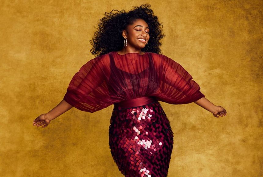 A young Black woman wears a designer sequined dress and lets the wind blow through her hair during a photo shoot.