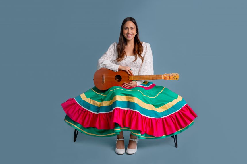 A smiling woman in a full skirt sits on a bench and holds a small guitar.