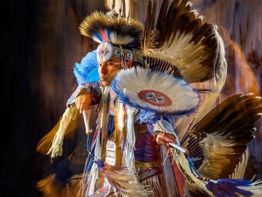 A Native American man dressed in full tribe regalia looks off into the distance.