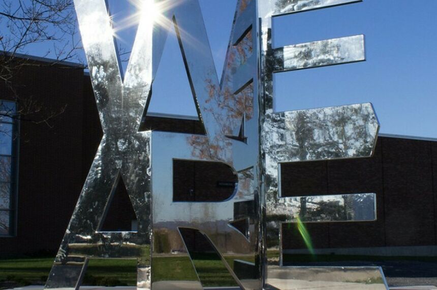 A mirrored statue in the shape of the words We Are reflects its surroundings.