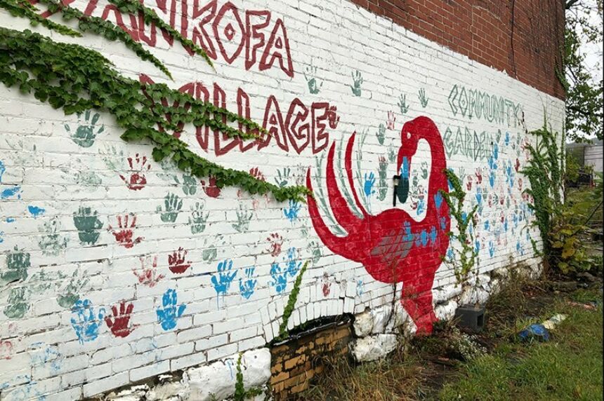 A brick wall that is painted white with a flamingo painted on it as well as Sankofa Village and the handprints of children in blue and red.