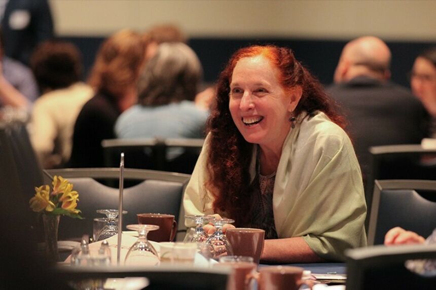 Woman with mid-length red hair seated at a table at a dinner smiling brightly
