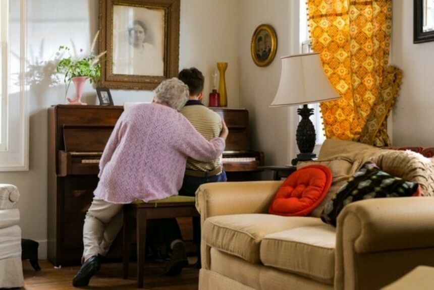 An elderly woman sitting on a piano bench hugging man next to her