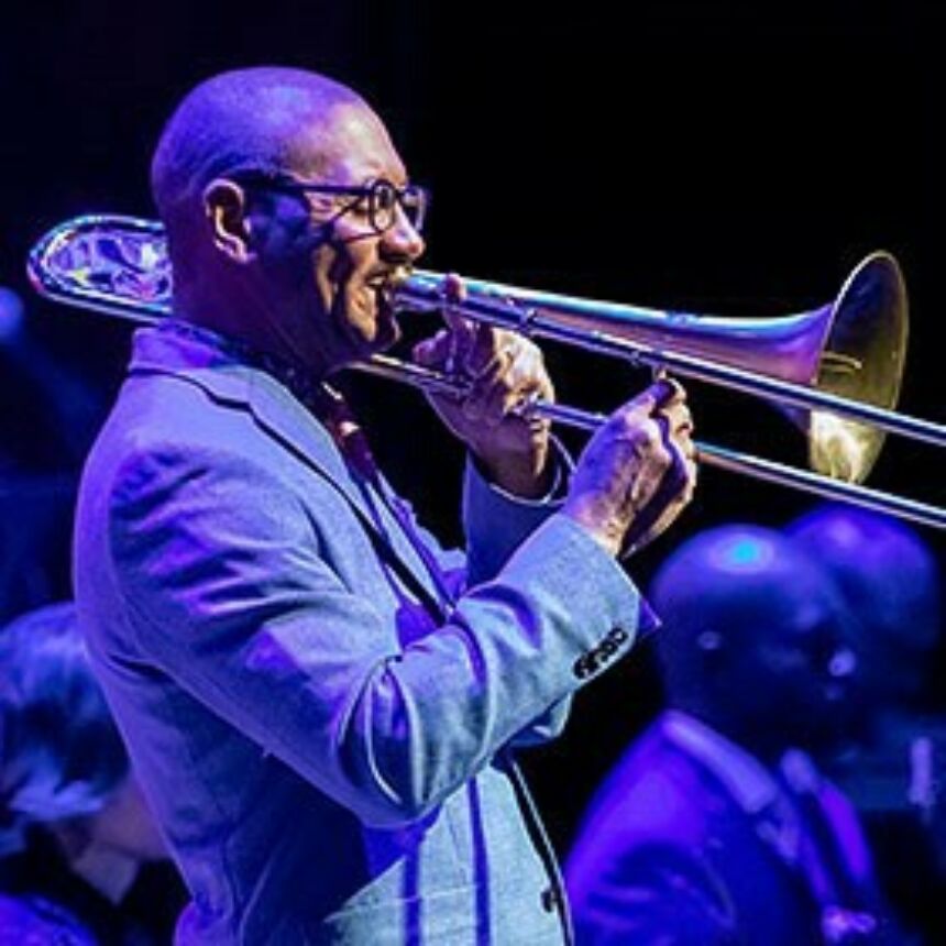 A man wearing a suit and eyeglasses plays s trombone.
