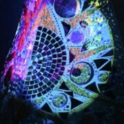 A mosaic tiled sculpture illuminated by a back light in the dark.