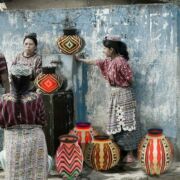 Photo of Guatemalan women conversing outside a house with several colorful woven containers.