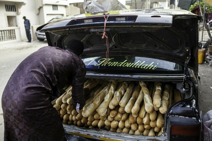 Man loading baguettes into the back trunk of a taxi for delivery.