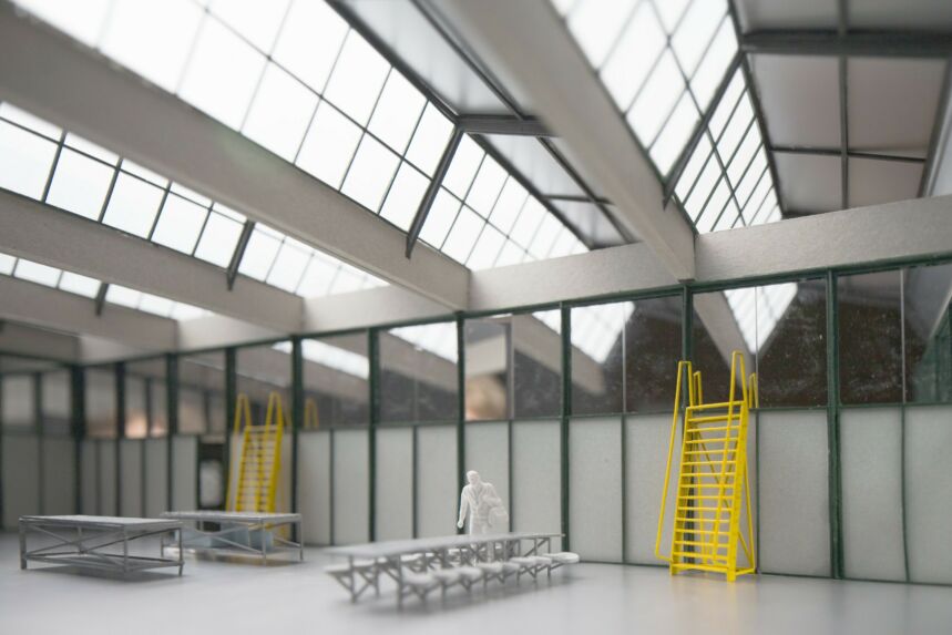 A model of a building with large rows of skylights in the ceiling, a row of windows atop the the wall, and two yellow ladders against the wall.