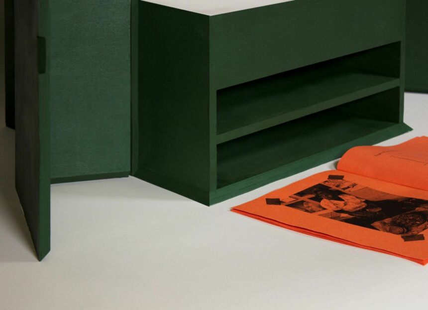 A green box with two compartments cut out. An orange publications is open in front of it.