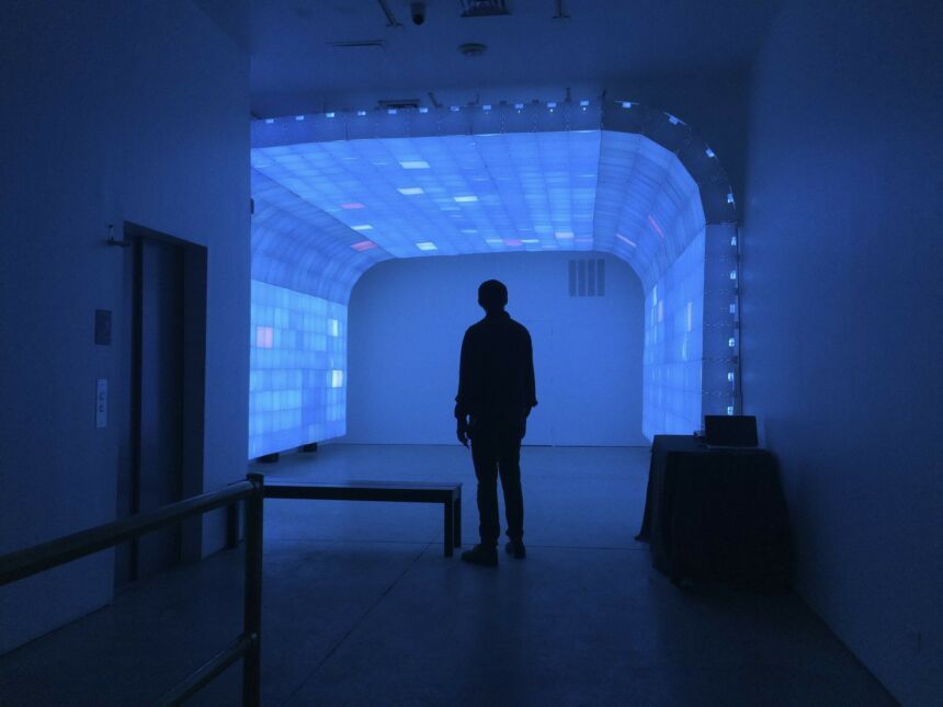 Silhouette of a man standing in room in front of an archway of blue light boxes.