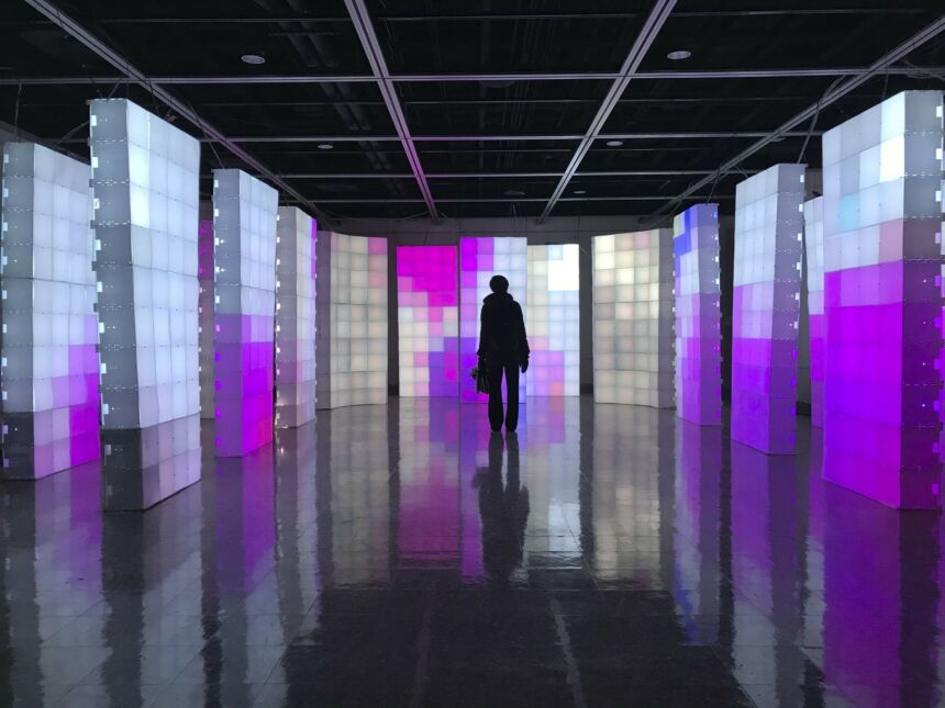 Silhouette of a person surrounded by many panels comprised of white, pink, blue, and purple light boxes.