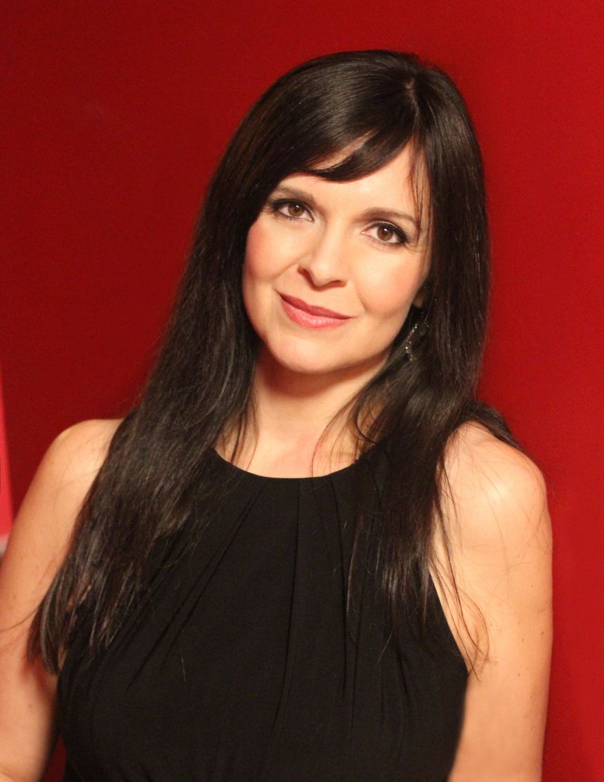 Dawn Pierce wearing black sleeveless dress black in front of deep red background.