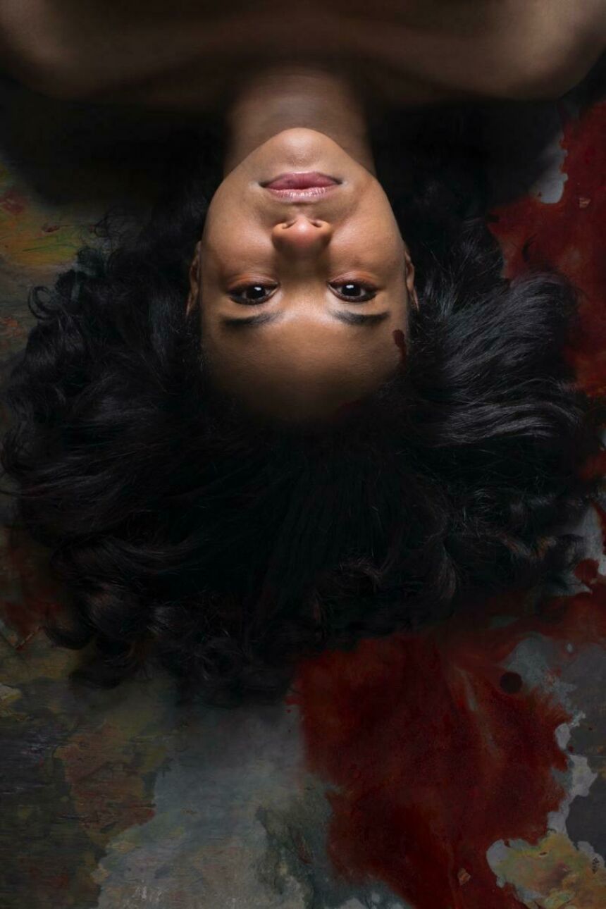 Head shot of a young woman of color lying upside-down against a dark, colorful abstract background.