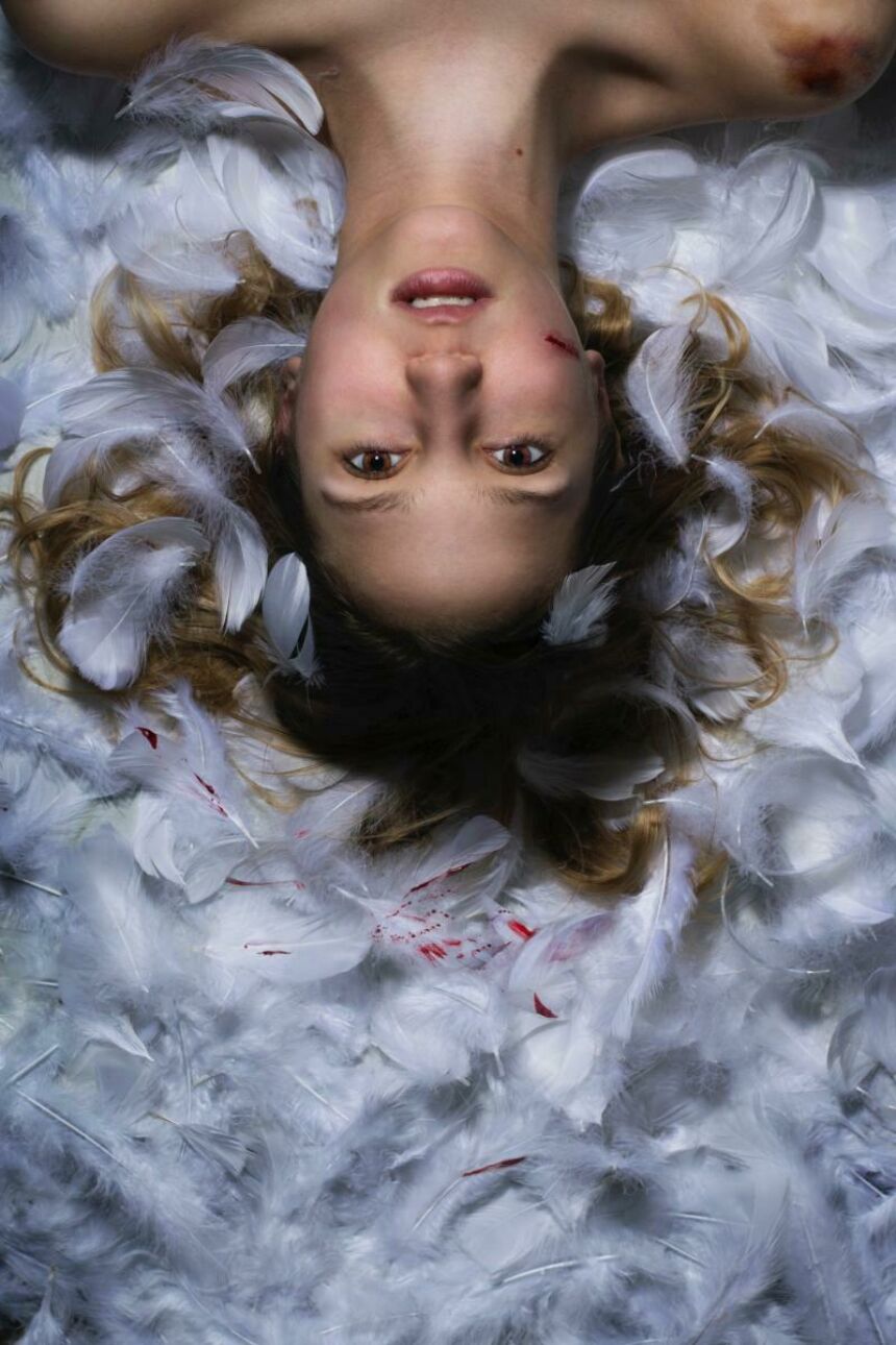 Head shot of a young injured woman lying in upside-down position, with a bit of blood staining the angel wings behind her.