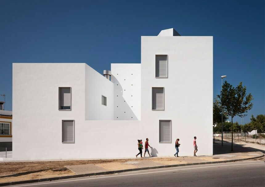 All-white housing unit building with four people walking on the sidewalk in front of it.