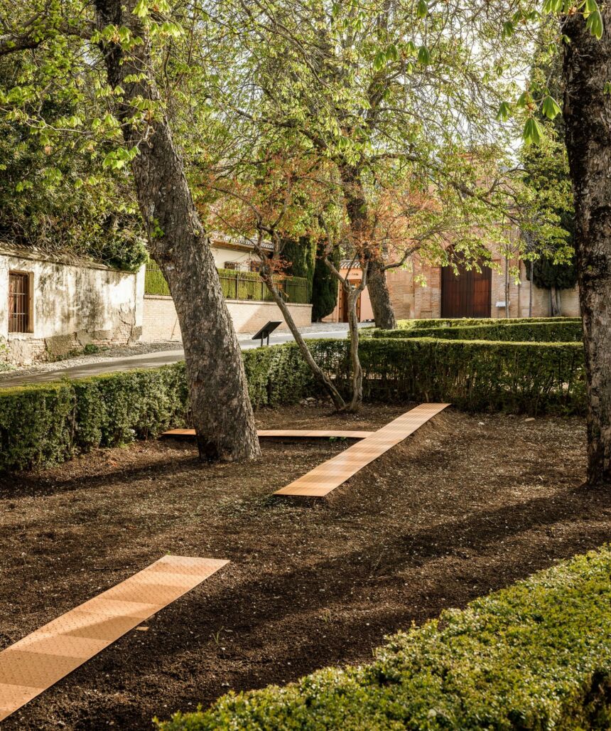 Outdoor garden area featuring large trees and hedges behind a house.