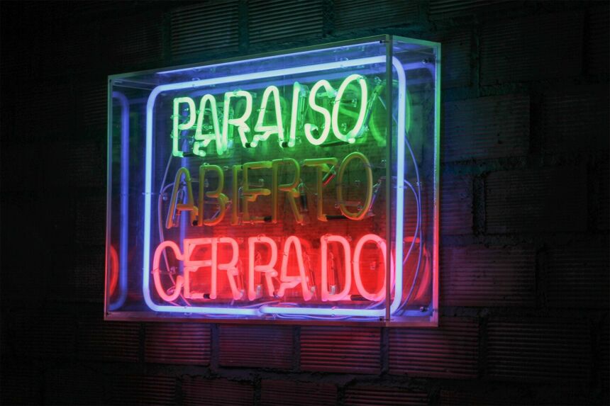 A neon sign at night that reads PARAISO in green; ABIERTO in non-lit lighting; and CERRADO in pink with a purple neon light border.