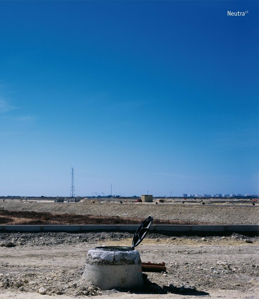 A blue sky behind a dry landscape with an open manhole remaining as the road around it is destructed.