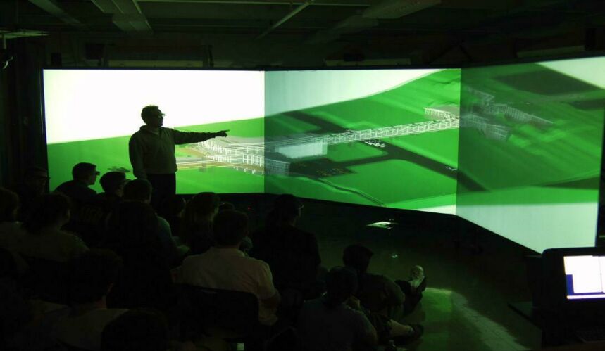 Photo of students observing a lecture with a panoramic projection of a computer-generated building design.