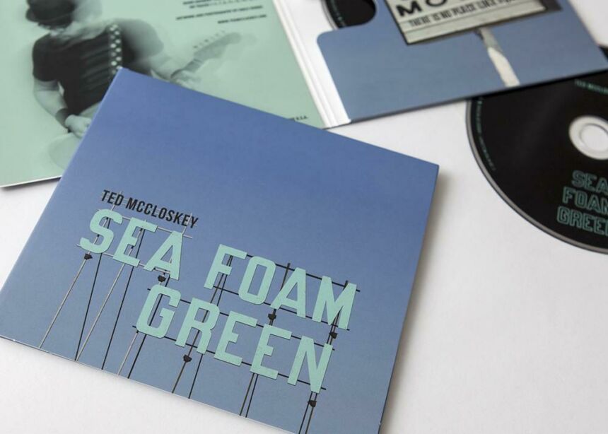 CD album art featuring "Ted McCloskey Sea Foam Green" signage against clear sky background. Open CD album is sitting behind, revealing artwork of more signage, a photo of Ted McCloskey, and a copy of his CD.