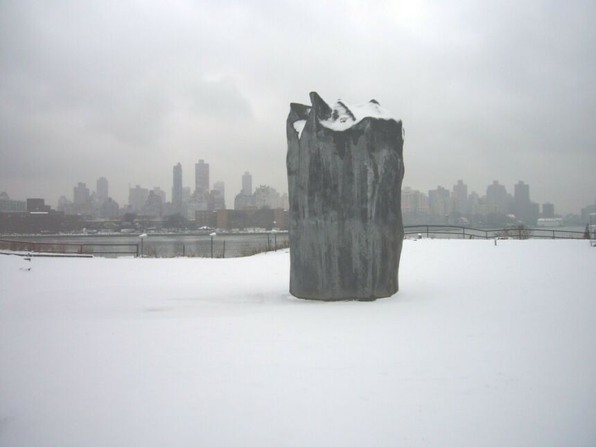 Tall dark grey sculpture set alone in a snowy field, with New York City's skyline in the background.