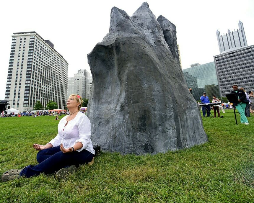 Woman meditating at the base of a large black rock sculpture.