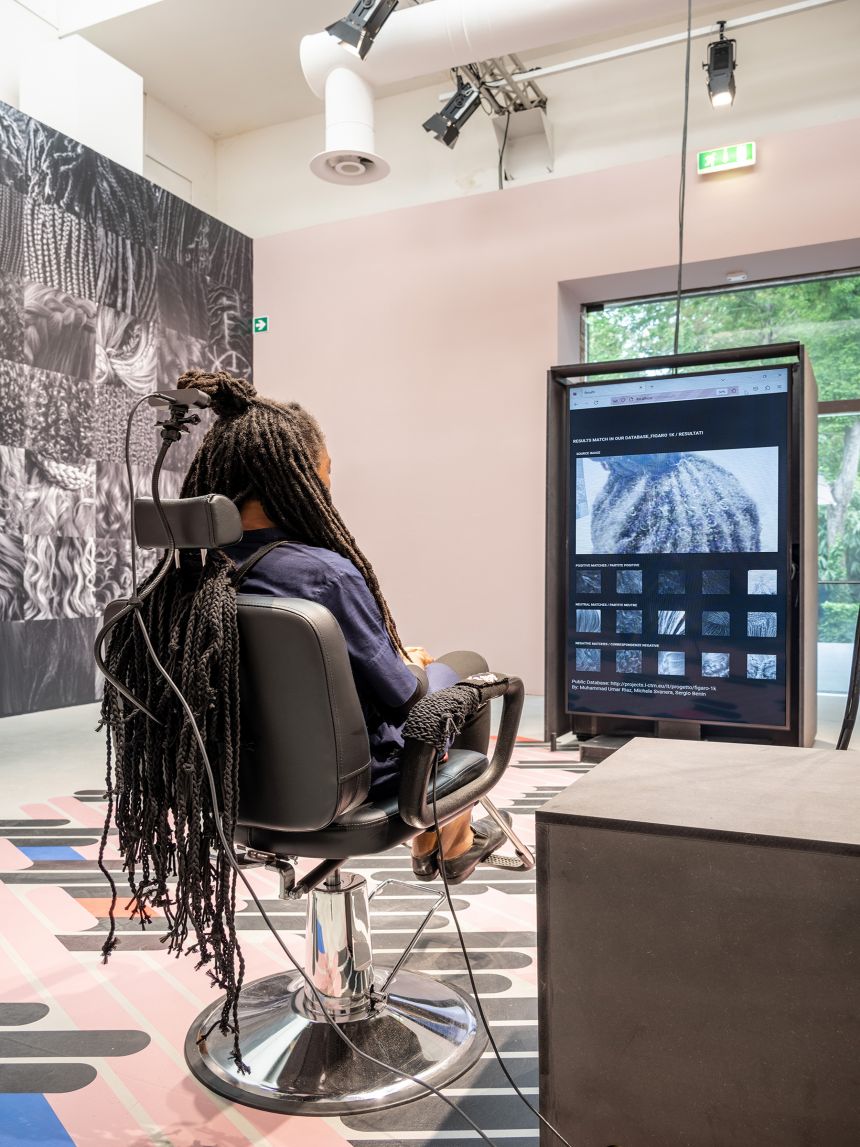 Felecia Davis sits in a hair salon chair in front of a screen with an image of her braided hair style projected on a screen before her.