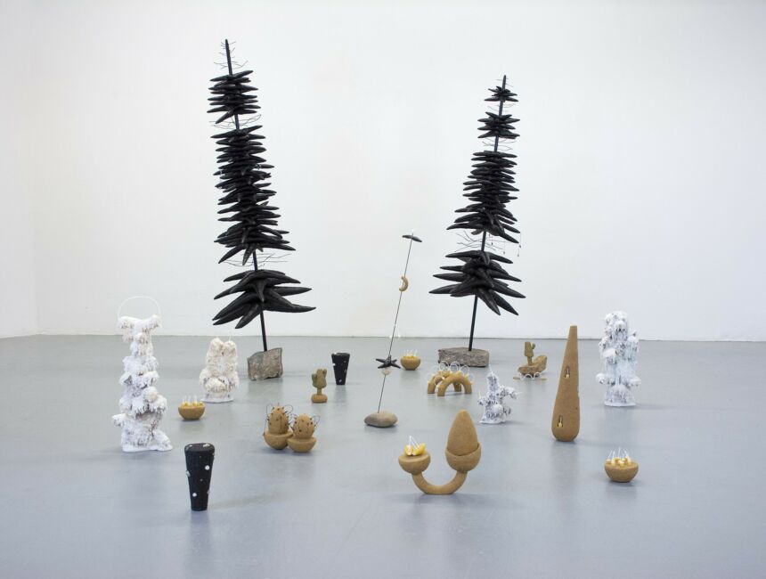 A collection of small abstract sculptures and two large pine tree sculptures in a white room.