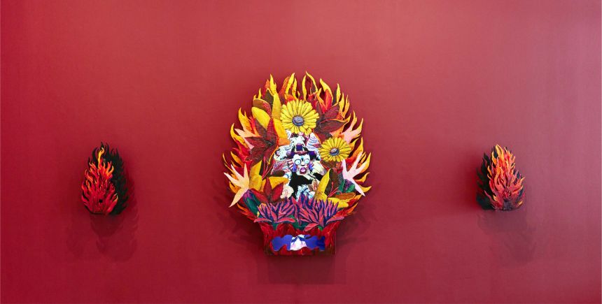 Three colorful, fiery sculptures displayed against a deep red wall.