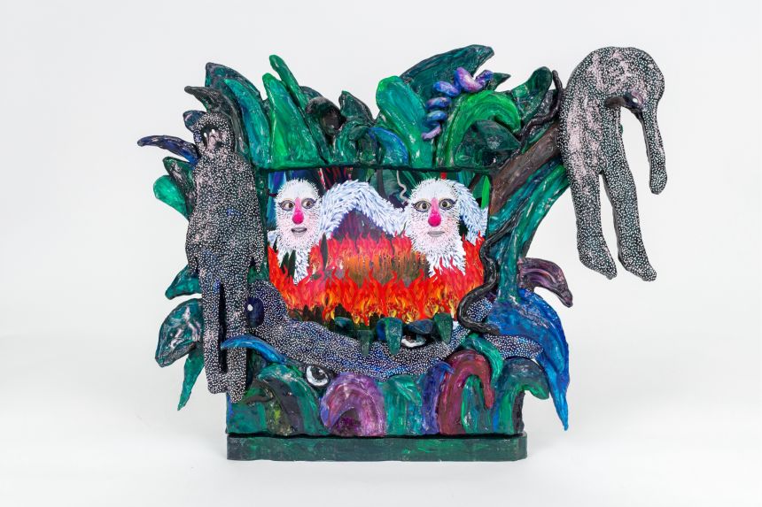 An elaborate sculpture with a performance stage and friendly white-furred monsters holding each other's upraised hands; the stage is sandwiched between foreground and background layers of plants, flowers and trees.