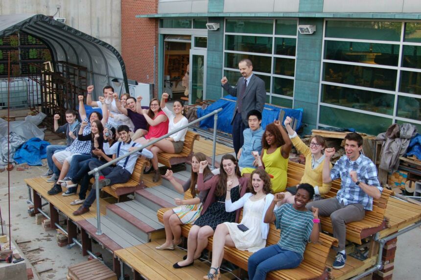 Overhead photo of Stuckeman students and one of the faculty members sitting on the bleachers and cheering with fists raised in the air.