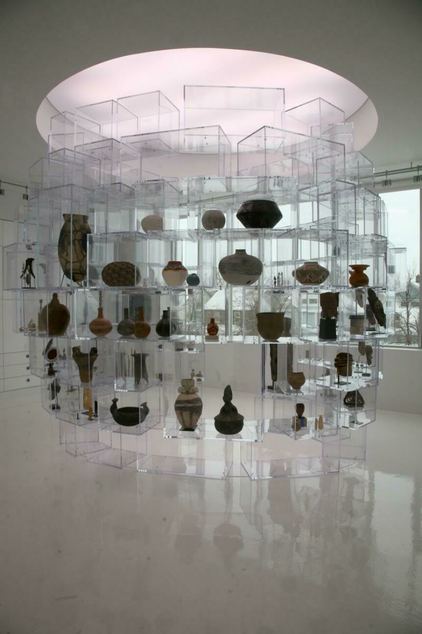 Interior shot of a white gallery with pottery sitting in acrylic block shelving, which are arranged in a circle.