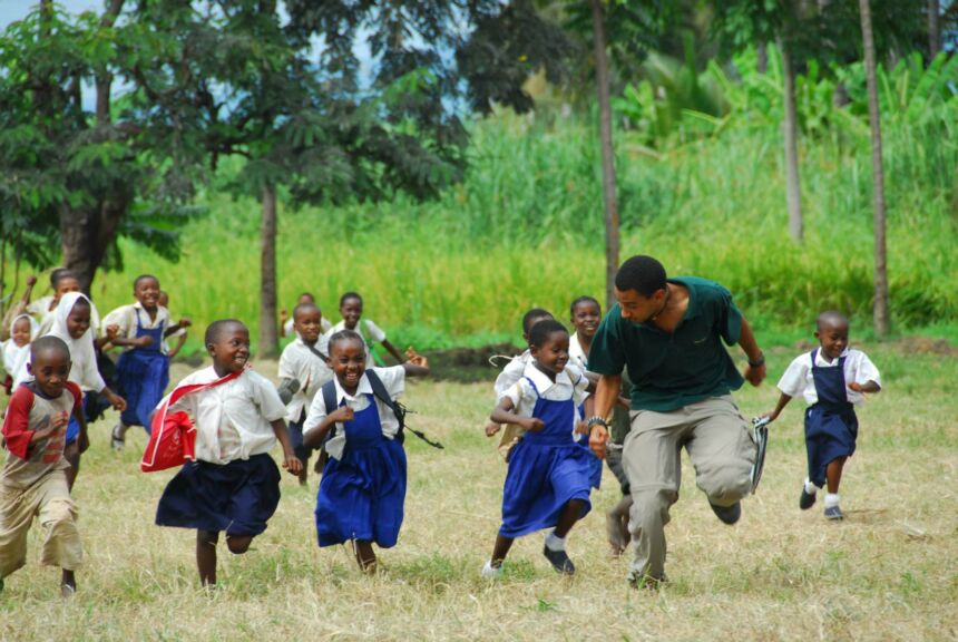 Photo of adult man running alongside smiling and laughing school children.