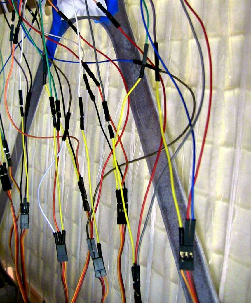 Photo of white, red, orange, yellow, green, and blue interconnected wires dangling from the back of the fabric panels.