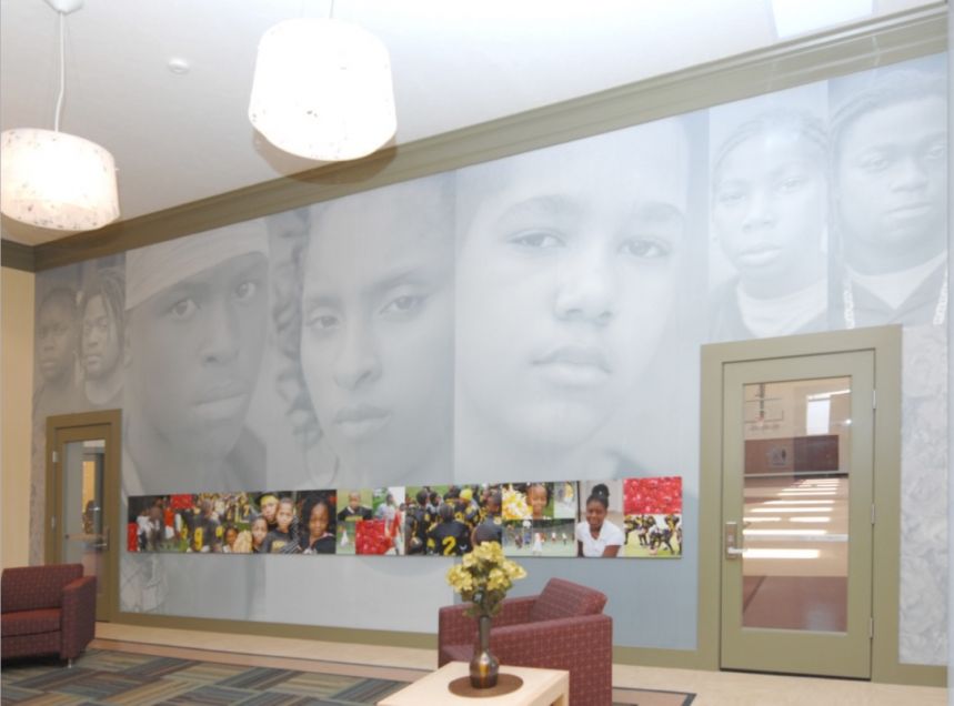 Large wall in room showing large format images of people as the wall-covering, with a smaller row of images stretching between two doors.
