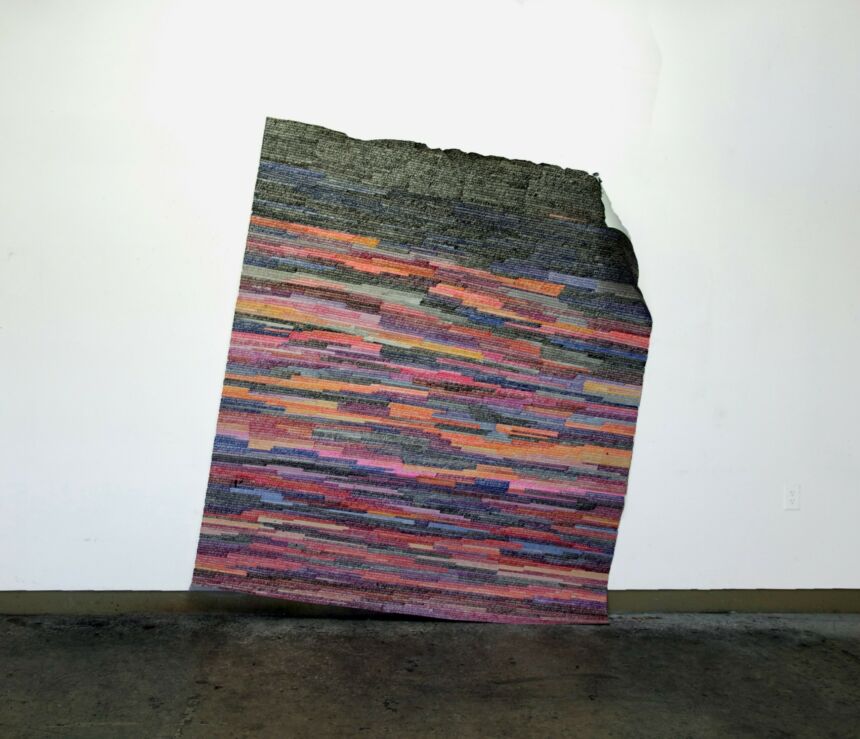 Photo of a large scale painting in multi-neon and black colors on folded paper hanging at an angle near the floor.