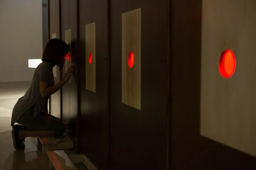 Cristin Millett peering through one of the red portholes of her "Coronal Plane" installation piece.