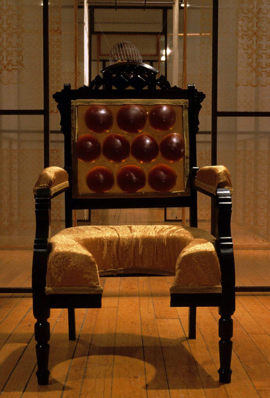Dark-stained wood throne, accented with gold jacquard padding on the arms and seat. The seat is cut out in a horseshoe shape and the backrest is adorned with ten dark red resin bumps.