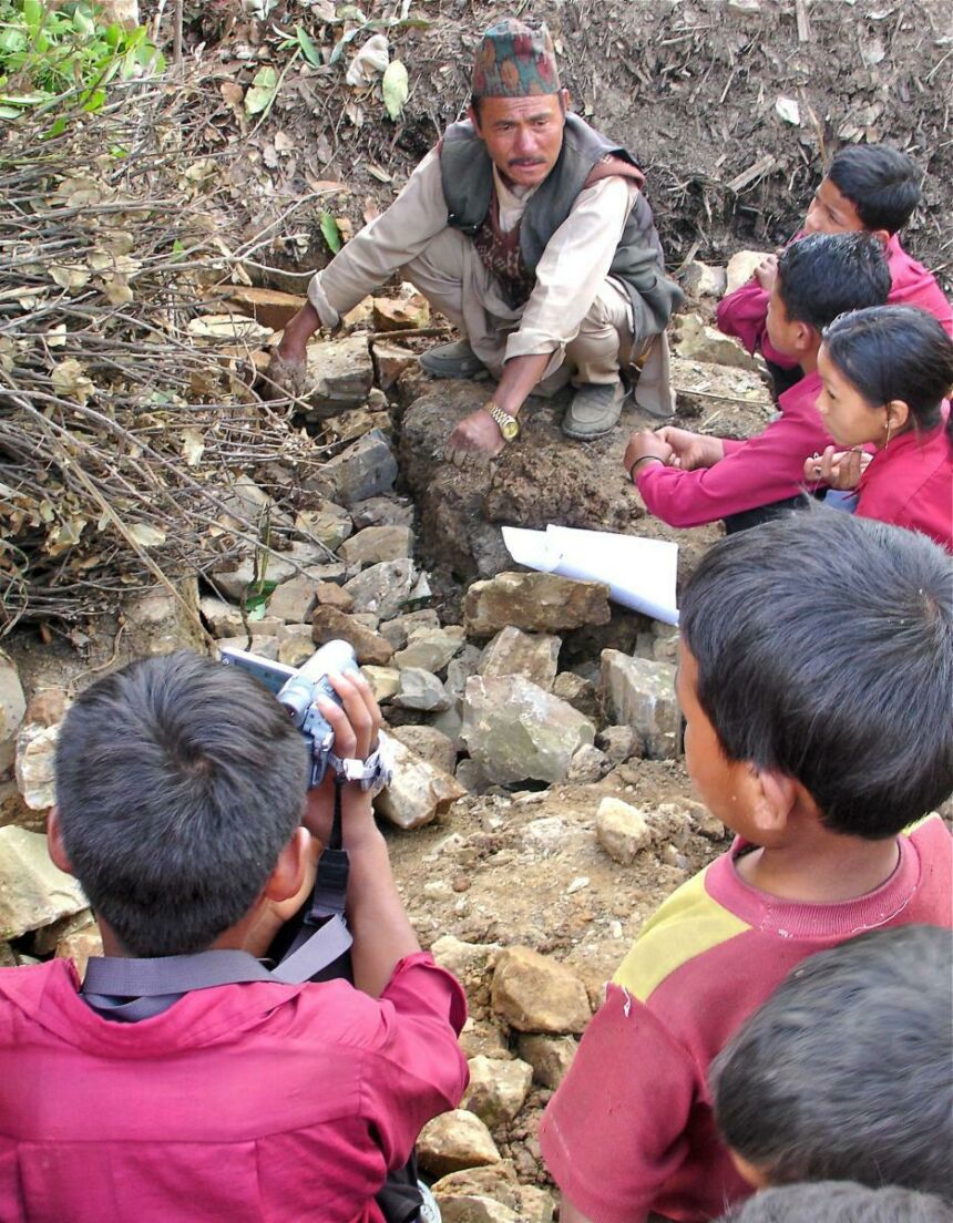 Photo of Nepali man crouching on a boulder lecturing a group of young students.